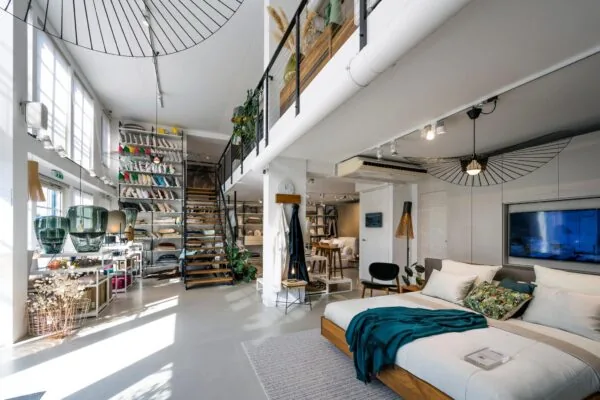 Modern ingerichte showroom aan de Oostelijke Handelskade met een bed, decoratieve kussens en een open trap naar een bovenverdieping.